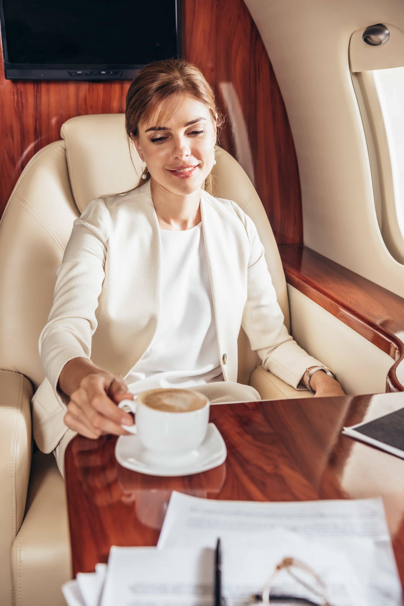 Woman smiling while holding a coffee cup inside a private jet cabin
